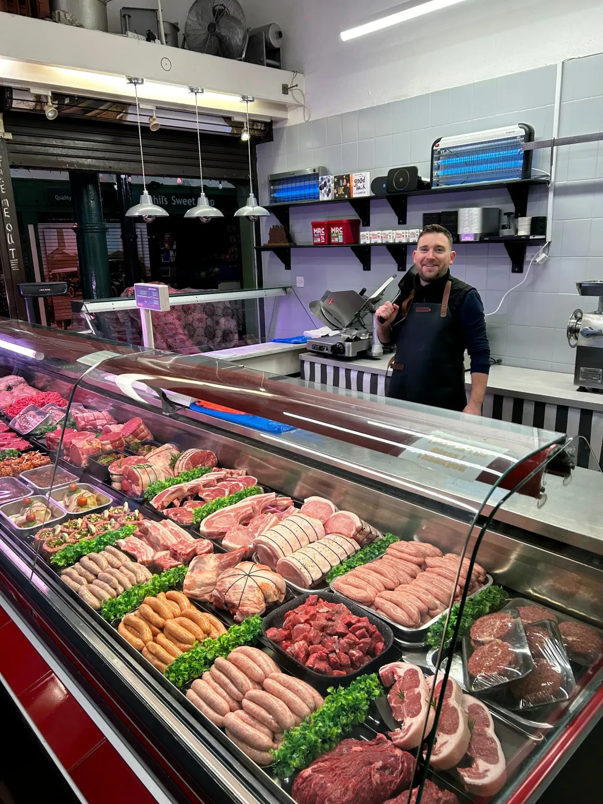 Lee, master butcher, holding a cleaver behind his meat counter at The Butchers Blade, Sandbach