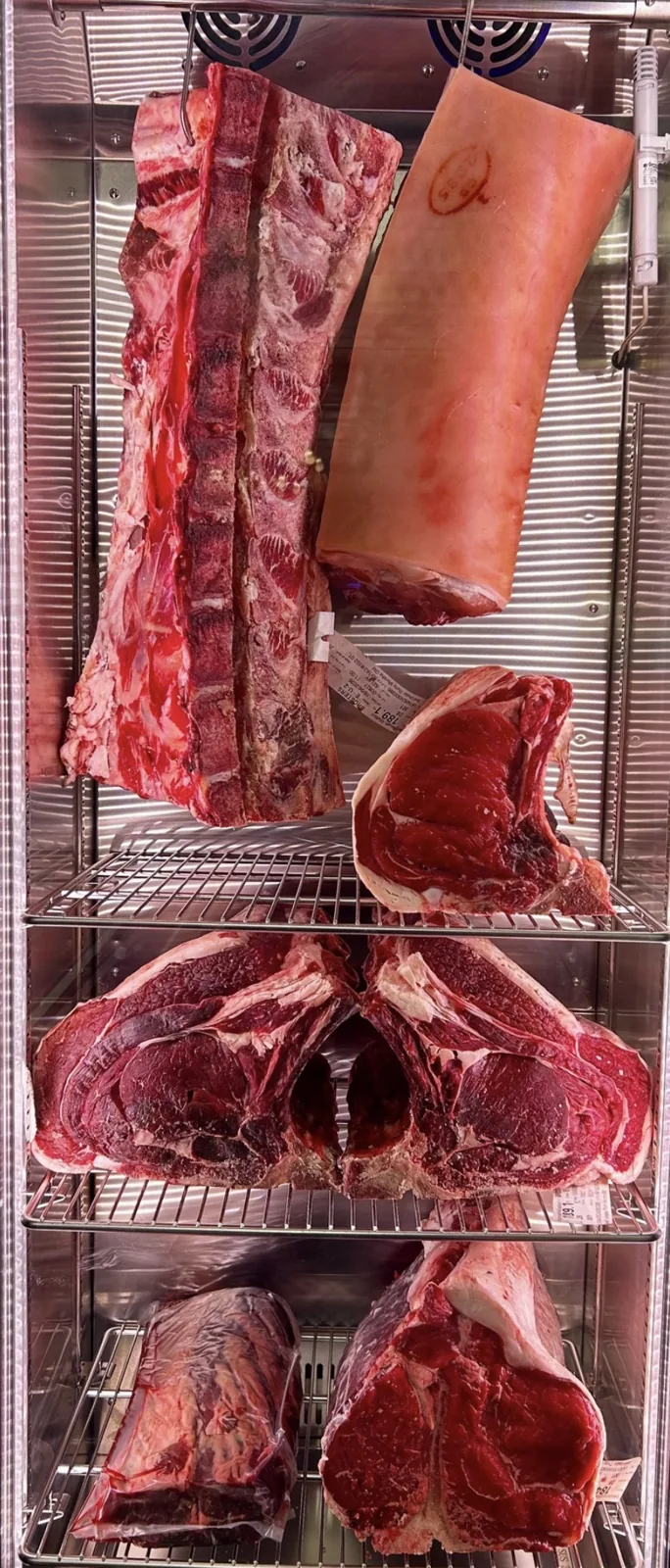 Close-up of dry-aged bone-in beef cuts in the shop’s dry-aging cabinet